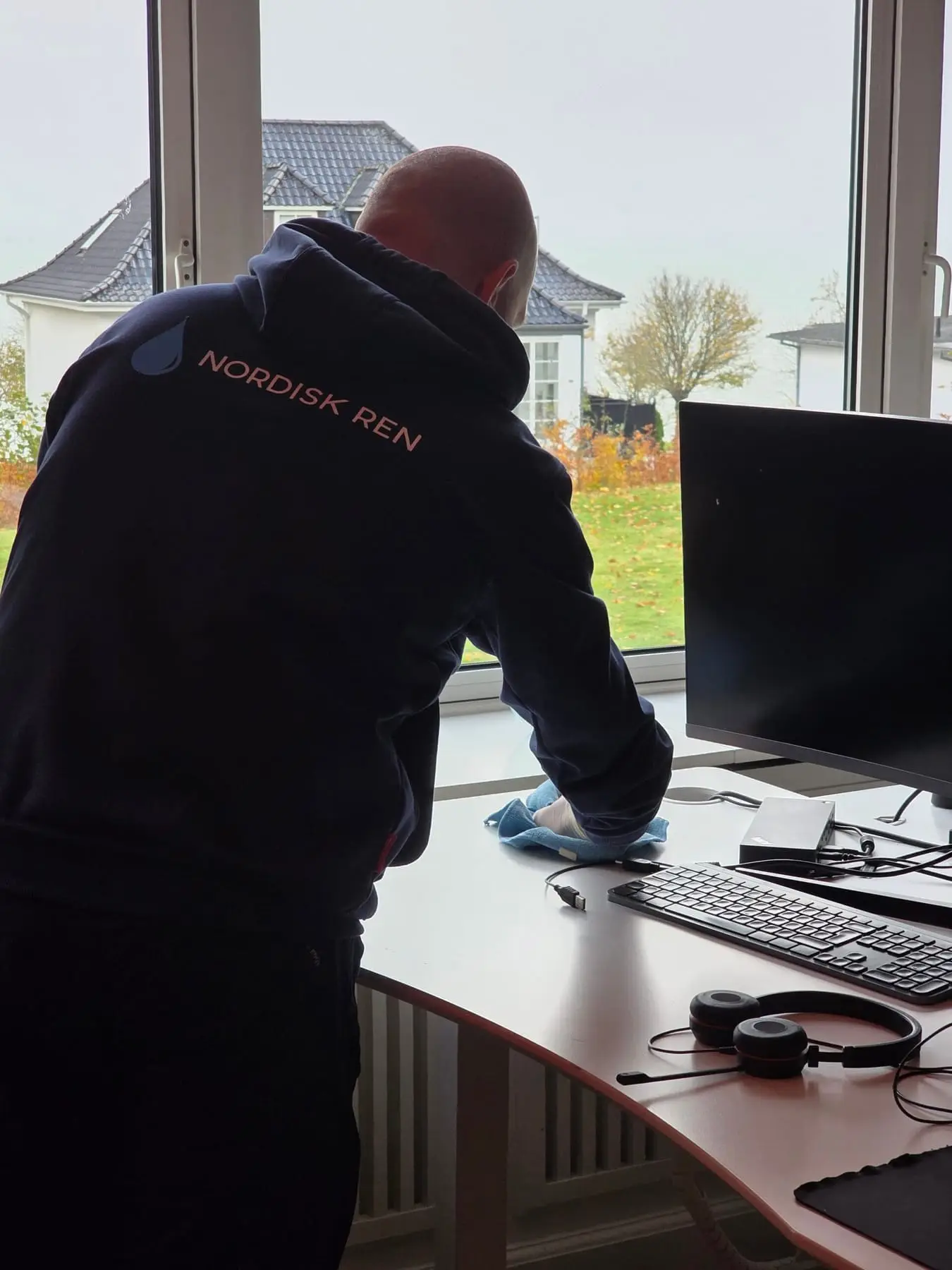 Person rengør skrivebord ved vindue i kontor
