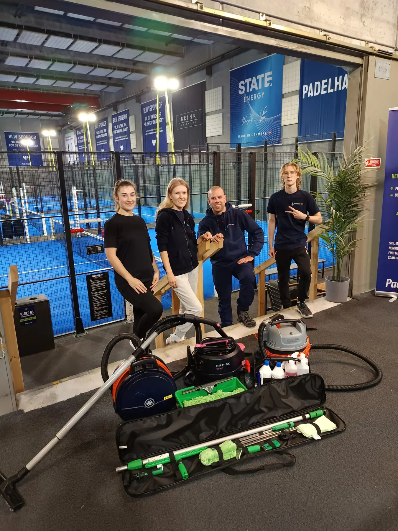 Fire personer ved padelbane med rengøringsudstyr
