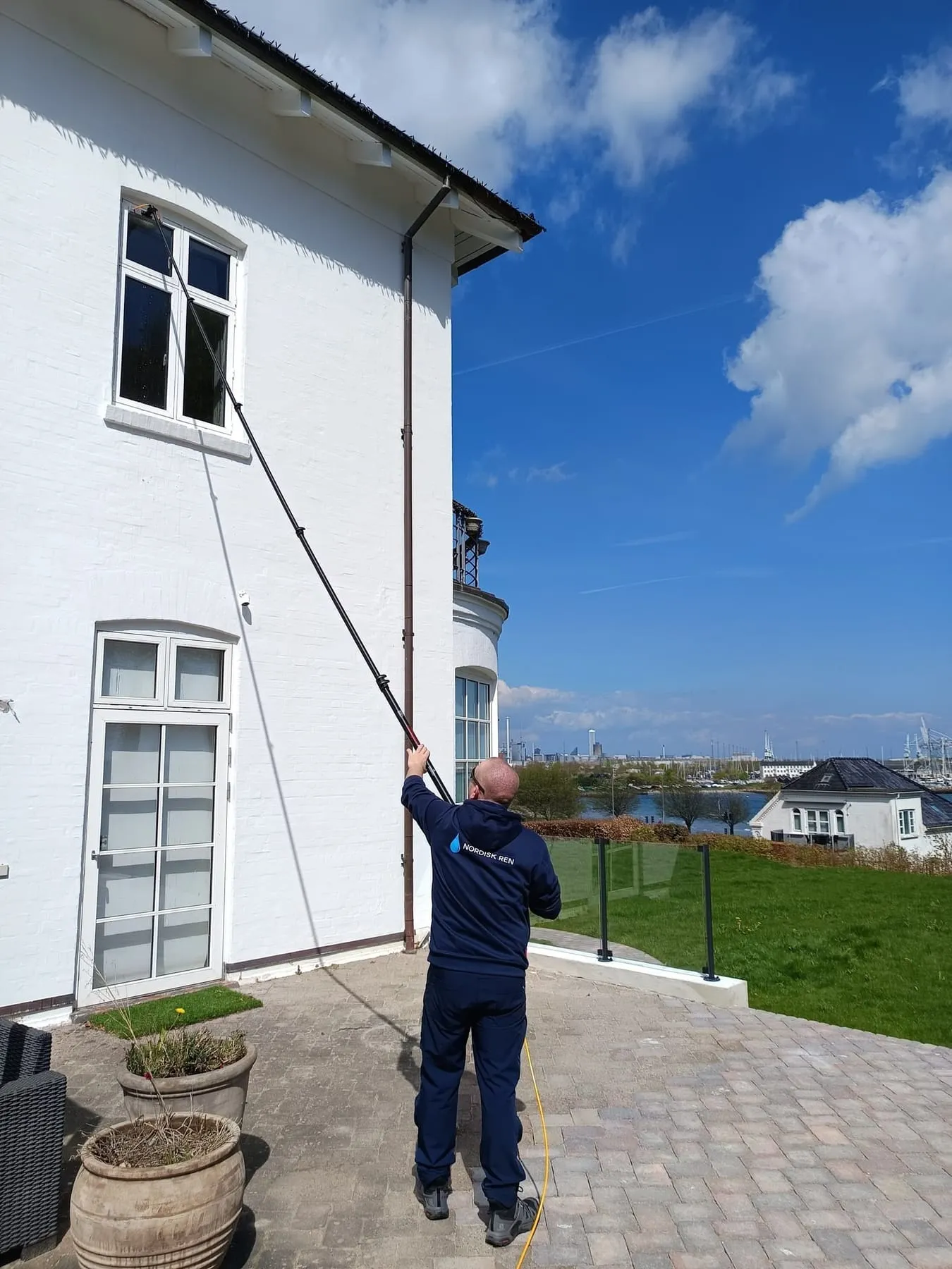 Mand rengør vindue med teleskopstang på hvid villa